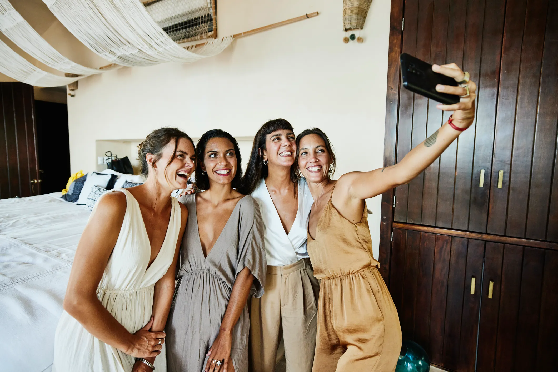 Medium wide shot of smiling and laughing bridesmaids tasking selfie in luxury hotel suite before wedding