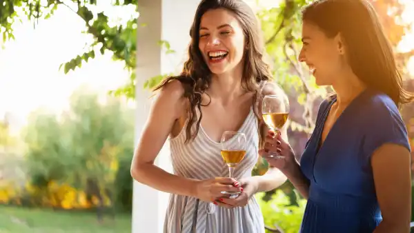 Serene female Caucasian friends, drinking wine while having a casual conversation during summer garden party