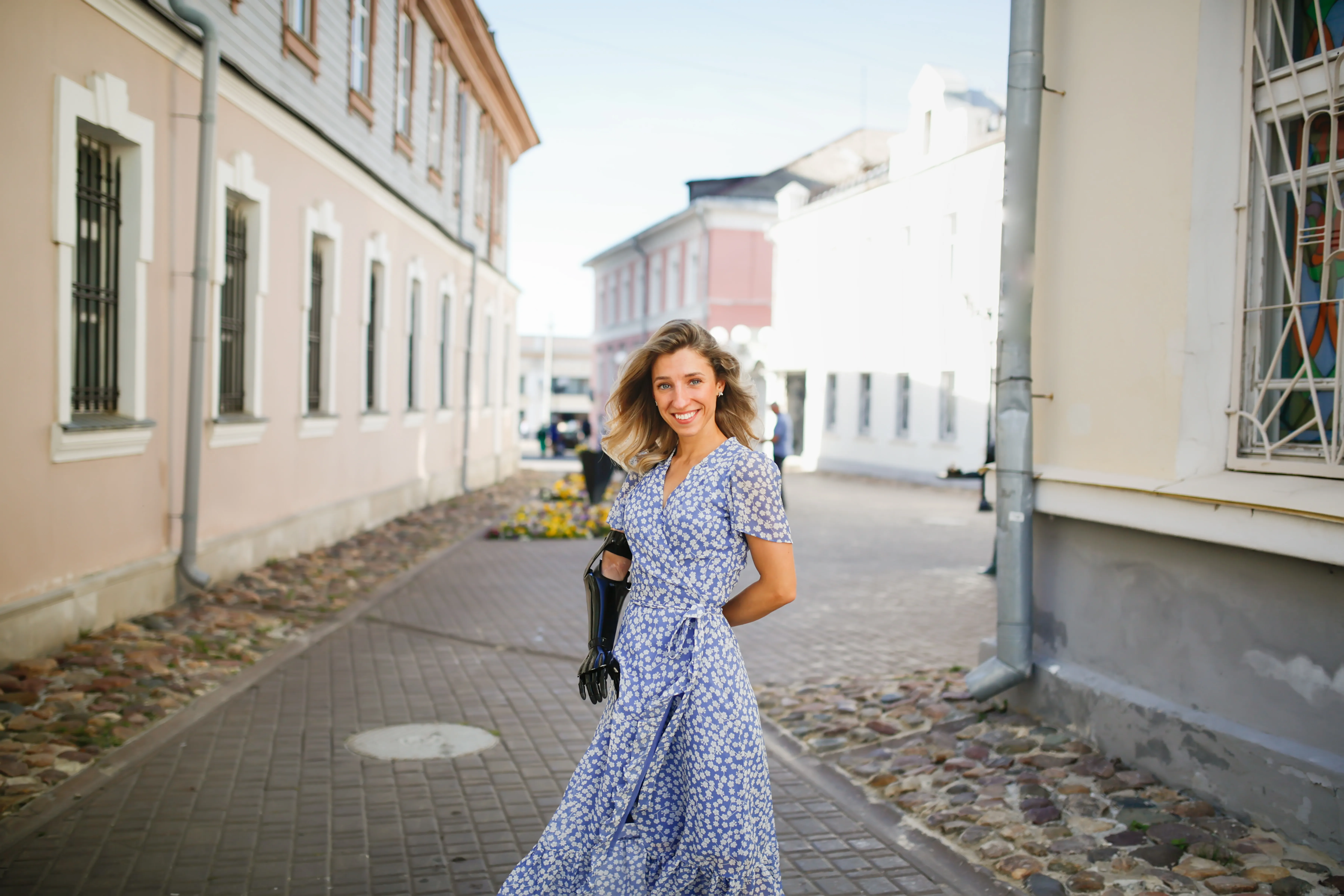 beautiful young slim woman in summer blue dress dance and walks through small town, local tourism