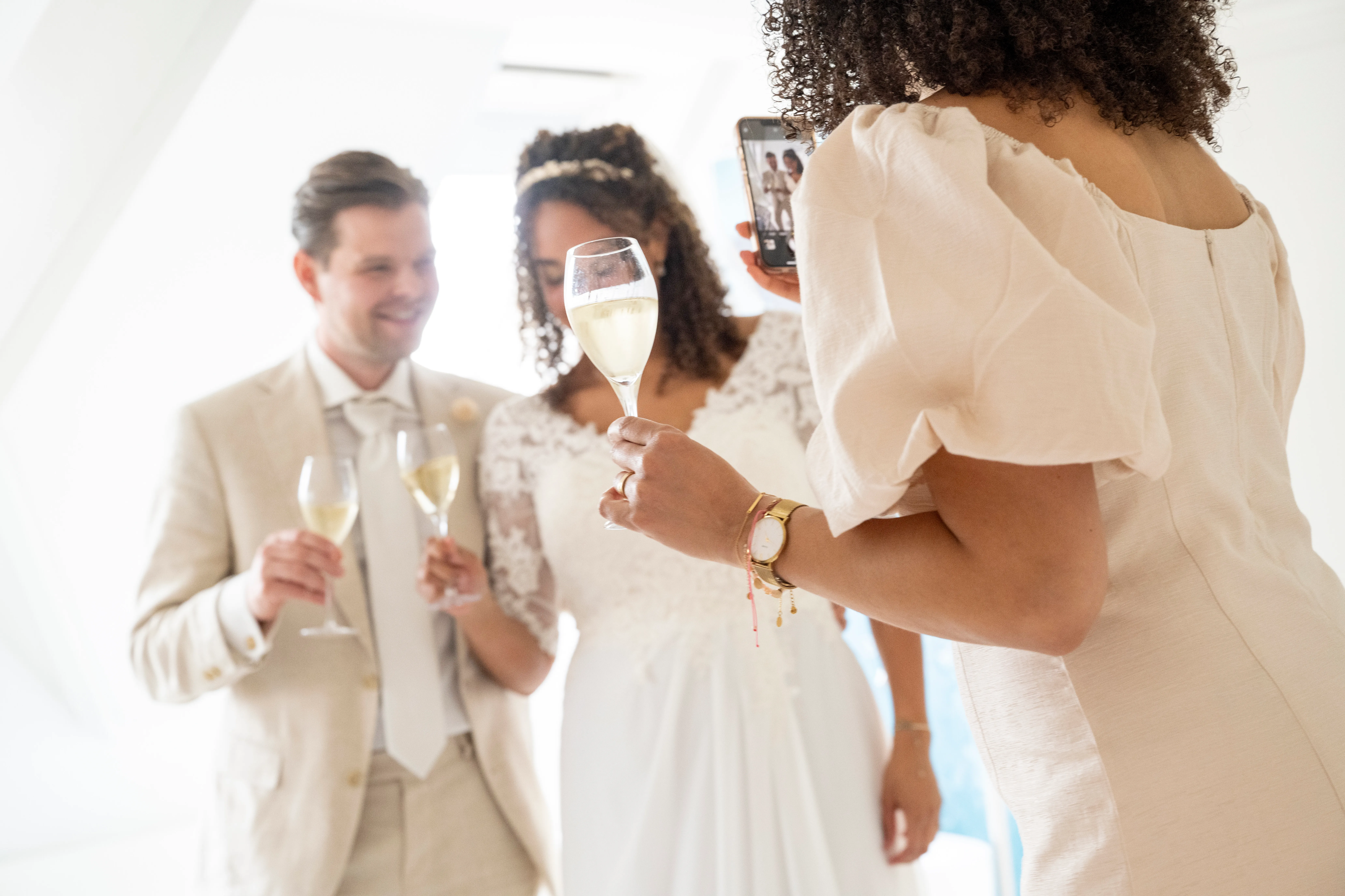 Bride and groom holding champagne glasses with a guest at a wedding celebration, sharing a toast