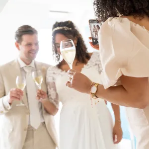 Bride and groom holding champagne glasses with a guest at a wedding celebration, sharing a toast