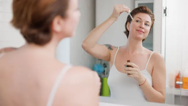 Beautiful middle-aged woman applying serum for facial care with pipette in front of the mirror - stock photo
