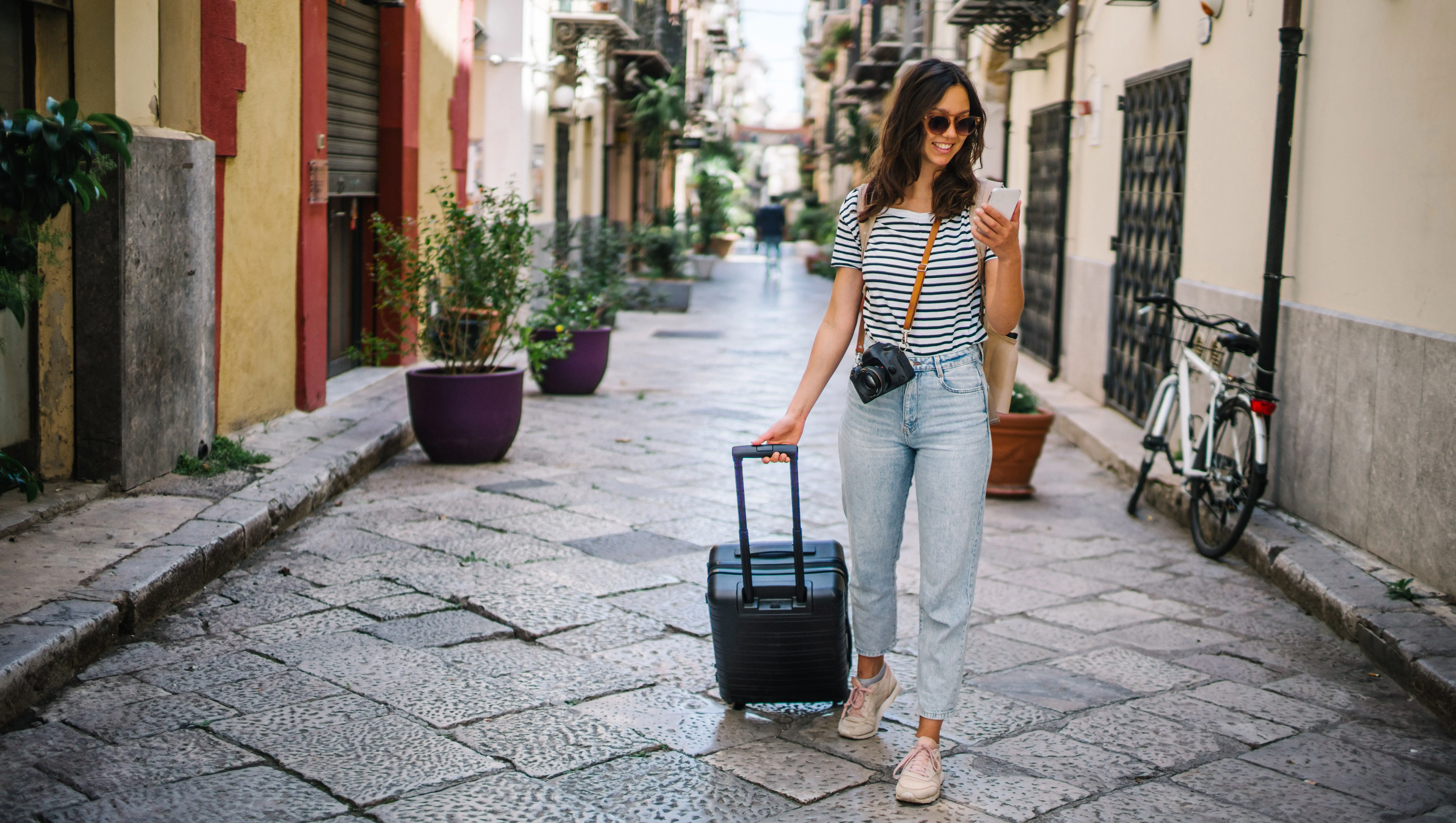 Young woman pulls suitcase down cobblestone street - stock photo