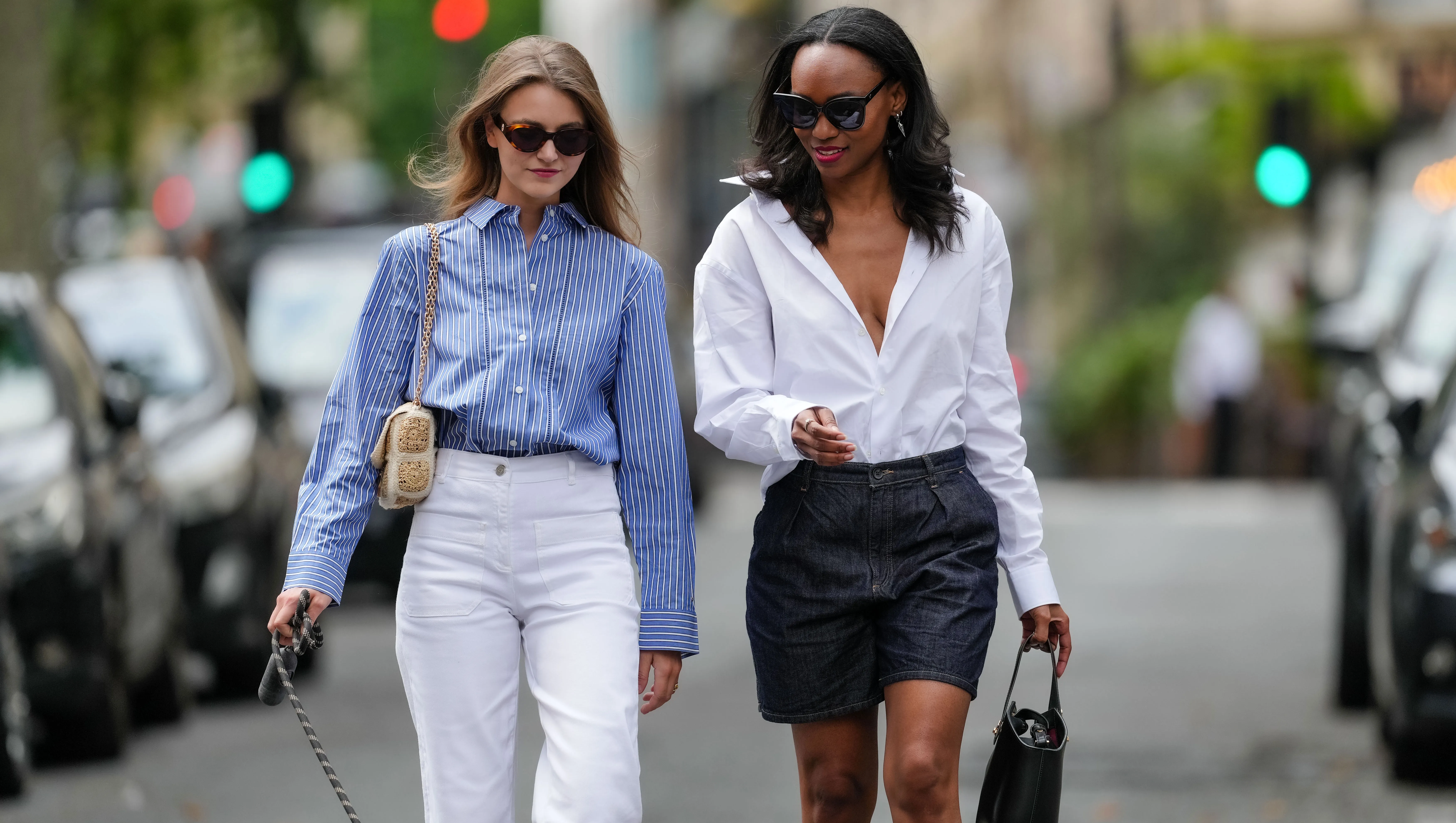 PARIS, FRANCE - MAY 20: Segolene Hyppolite (L) wears sunglasses, a blue and white oversized shirt from Tommy Hilfiger, a raffia beige bag from Vanessa Bruno, high waist white denim pants from Vanessa Bruno ; Emilie Joseph (R) wears a summer wardrobe capsule: an oversized white poplin button-down shirt from Figaret Paris , tucked into high-waisted denim bermuda/ jorts / denim shorts, classic / basic / timeless accessories such as black sunglasses from the Korean fashion brand Gentle Monster, a small black top handle leather handbag, during a street style fashion photo session, on May 20, 2024 in Paris, France. (Photo by Edward Berthelot/Getty Images)