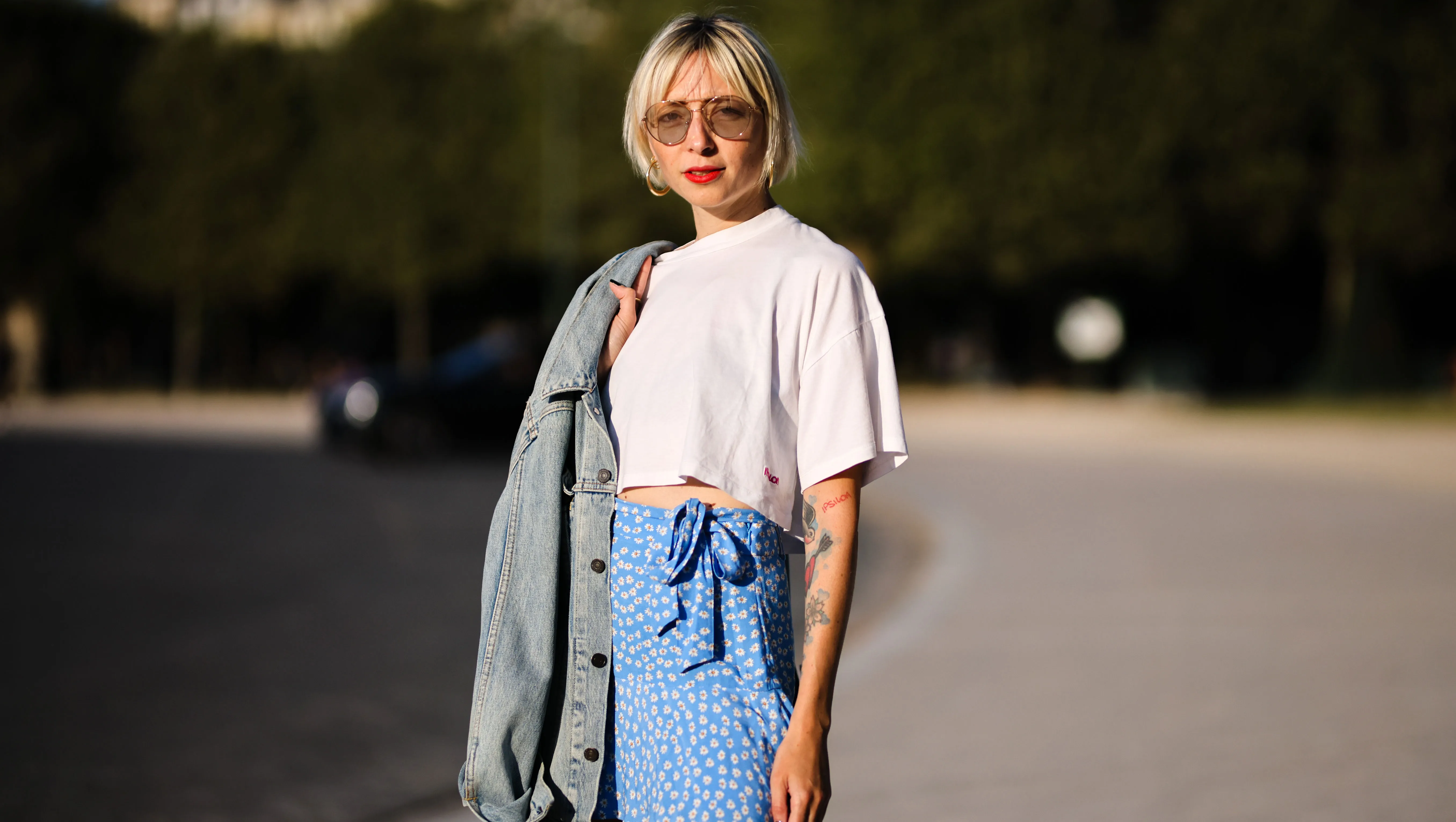PARIS, FRANCE - AUGUST 25: Emy venturini wears sunglasses from Prada, gold large earrings, a white cropped t-shirt from Ipsilon, a blue faded denim oversized long jacket, a blue with daisy flower print pattern flowing / high waist / knotted / short skirt from Zara, gold rings, on August 25, 2021 in Paris, France. (Photo by Edward Berthelot/Getty Images)