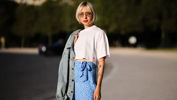 PARIS, FRANCE - AUGUST 25: Emy venturini wears sunglasses from Prada, gold large earrings, a white cropped t-shirt from Ipsilon, a blue faded denim oversized long jacket, a blue with daisy flower print pattern flowing / high waist / knotted / short skirt from Zara, gold rings, on August 25, 2021 in Paris, France. (Photo by Edward Berthelot/Getty Images)