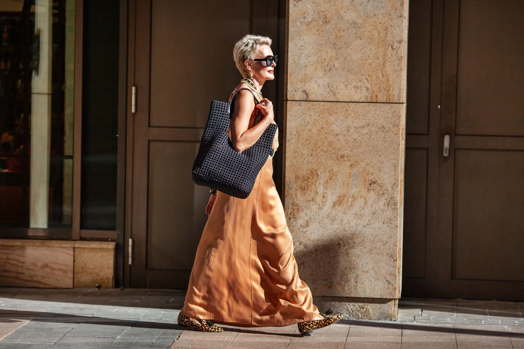 Stylish Mature Woman with Short Hairstyle Walks, Wearing Summer Beige maxi Dress and Large Handbag. Fashion Mode in City.