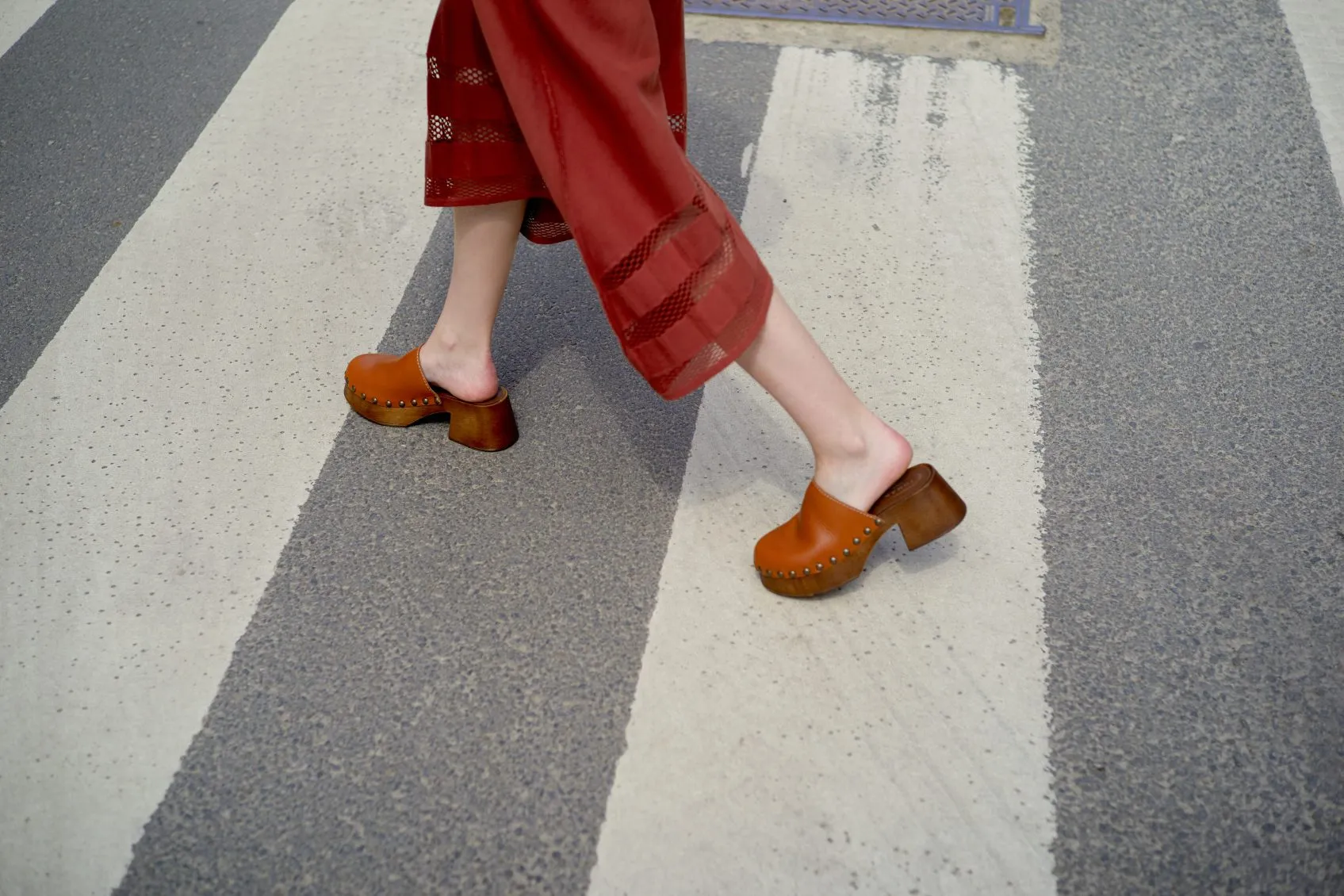 Person wearing red pants and brown clogs walking on a crosswalk. Brussels, Belgium
