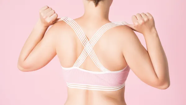Fit woman in sports bra on pink background, body care concept