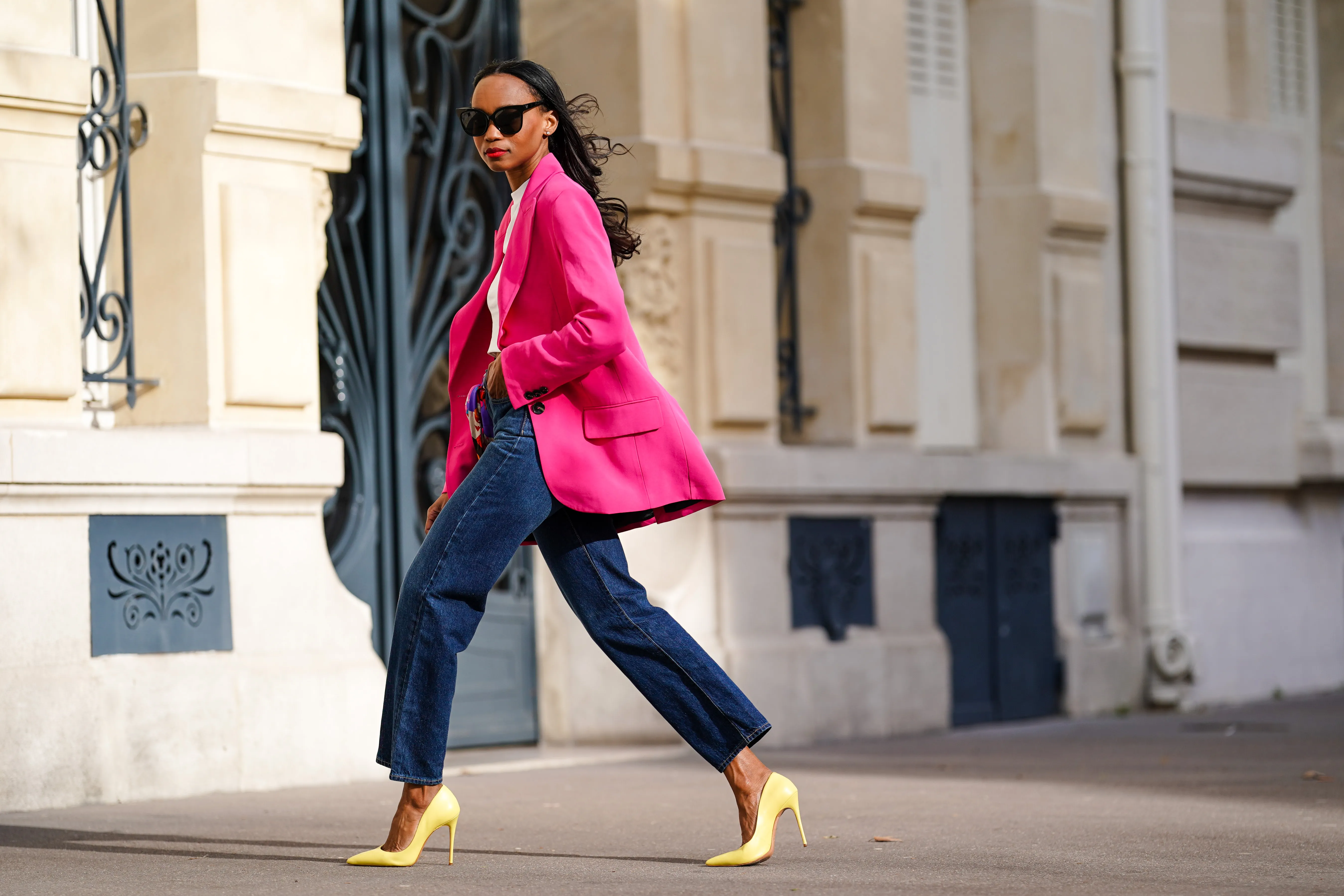 Emilie Joseph @in_fashionwetrust wears sunglasses, a bright neon pink oversized blazer jacket from Zara, a white crew neck crop top from H&M, high rise ribcage straight blue jeans in dark indigo from Levi's, a silk floral multicolor printed scarf worn as a belt from Kenzo, yellow high heels pointy stilettos shoes from Cosmoparis, on March 21, 2021 in Paris, France.