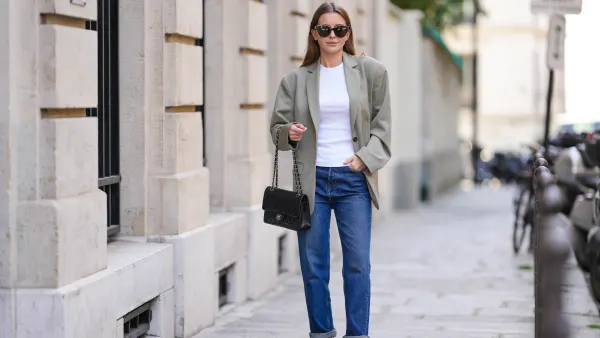 Diane Batoukina @diaanebt wears black sunglasses from Chanel, a white t-shirt, a beige gray oversized blazer jacket from Anine Bing, navy blue denim rolled-up large pants from Rouje, a black shiny grained leather Timeless handbag from Chanel, black shiny leather loafers mules from Massimo Dutti, during a street style fashion photo session, on April 15, 2022 in Paris, France.