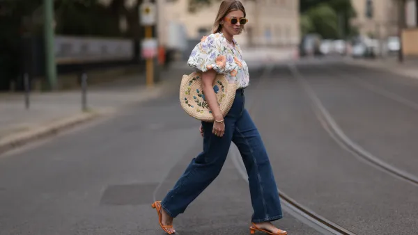 Aline Kaplan wearing Baum & Pferdgarten wide leg blue denim pants, & other stories white flower pattern cropped blouse and orange summer heels and Mango orange black shades on June 06, 2023 in Berlin, Germany.