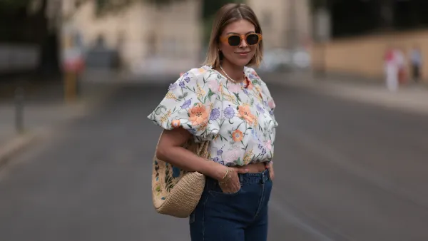 Aline Kaplan wearing Baum & Pferdgarten wide leg blue denim pants, & other stories white flower pattern cropped blouse and orange summer heels and Mango orange black shades on June 06, 2023 in Berlin, Germany.