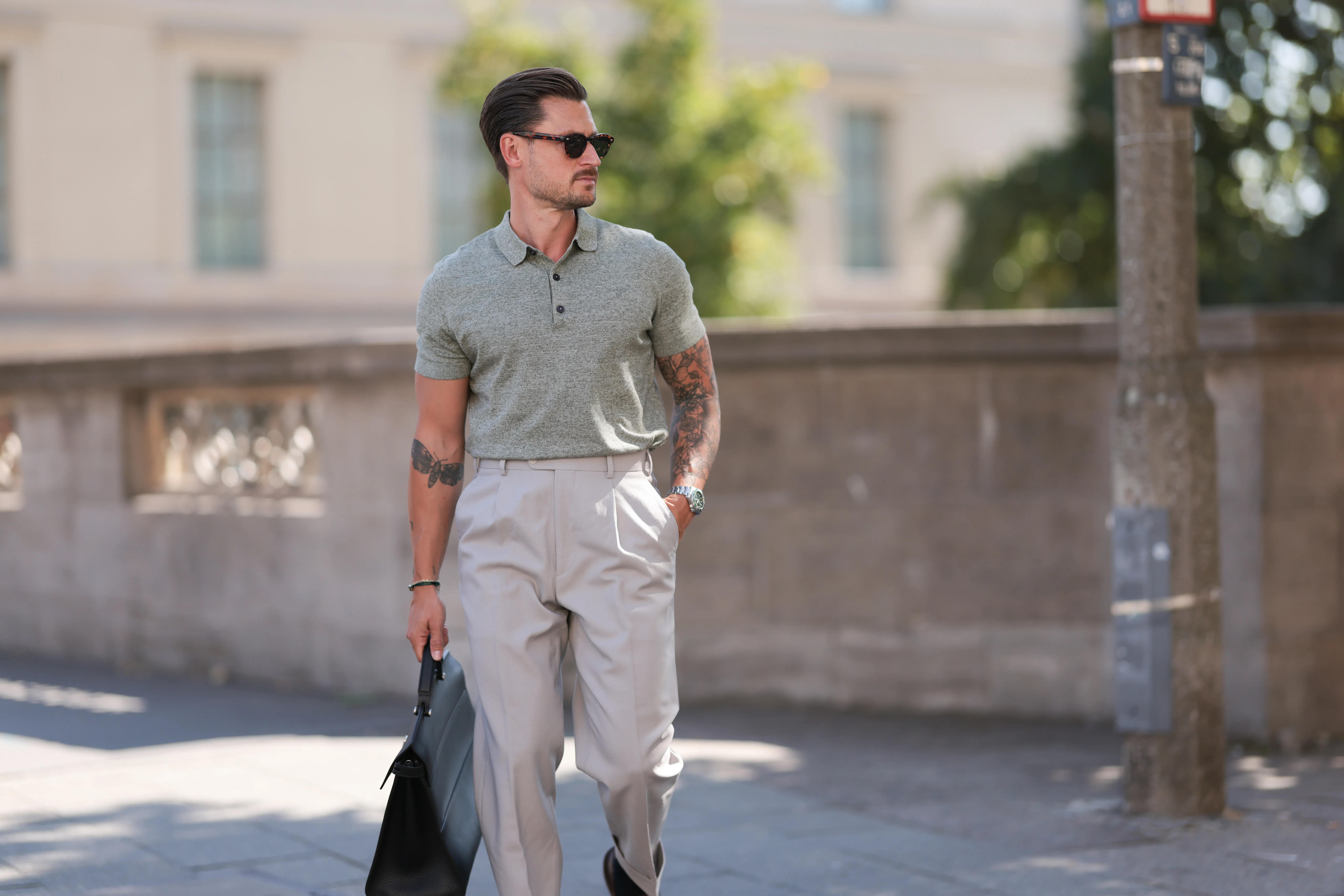 André Hellmundt seen wearing Explicit Poets brown sunglasses, Barbour sage green knit polo shirt, Suit Supply beige long suit pants, Tagheuer silver watch, Furla black leather briefcase / business bag and Bobbie’s Paris brown leather loafers, on August 27, 2024 in Berlin, Germany.