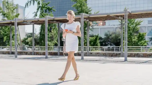 Young woman is strolling through a contemporary city, multitasking with her smartphone as she moves through the urban environment