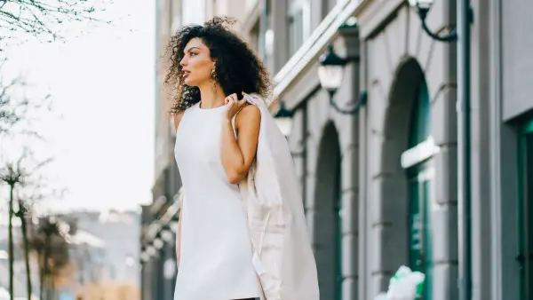 Stylish mixed race businesswoman walking down a city street, carrying her jacket over her shoulder
