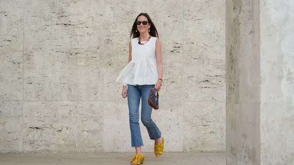 PARIS, FRANCE - MAY 02: Alba Garavito Torre wears black sunglasses, long straight brown hair with a center part, a white pleated peplum sleeveless blouse by Commense, and blue high-rise raw-hem denim jeans. A yellow clog sandal with floral detailing by AGL is worn, paired with a jean denim and brown mini Jackie handbag by Gucci. Accessories include a chunky necklace with colorful natural stones by Sempiterno Paris and gold jewelry. Full body shot, during a street style fashion photo session, on May 02, 2025 in Paris, France. (Photo by Edward Berthelot/Getty Images)