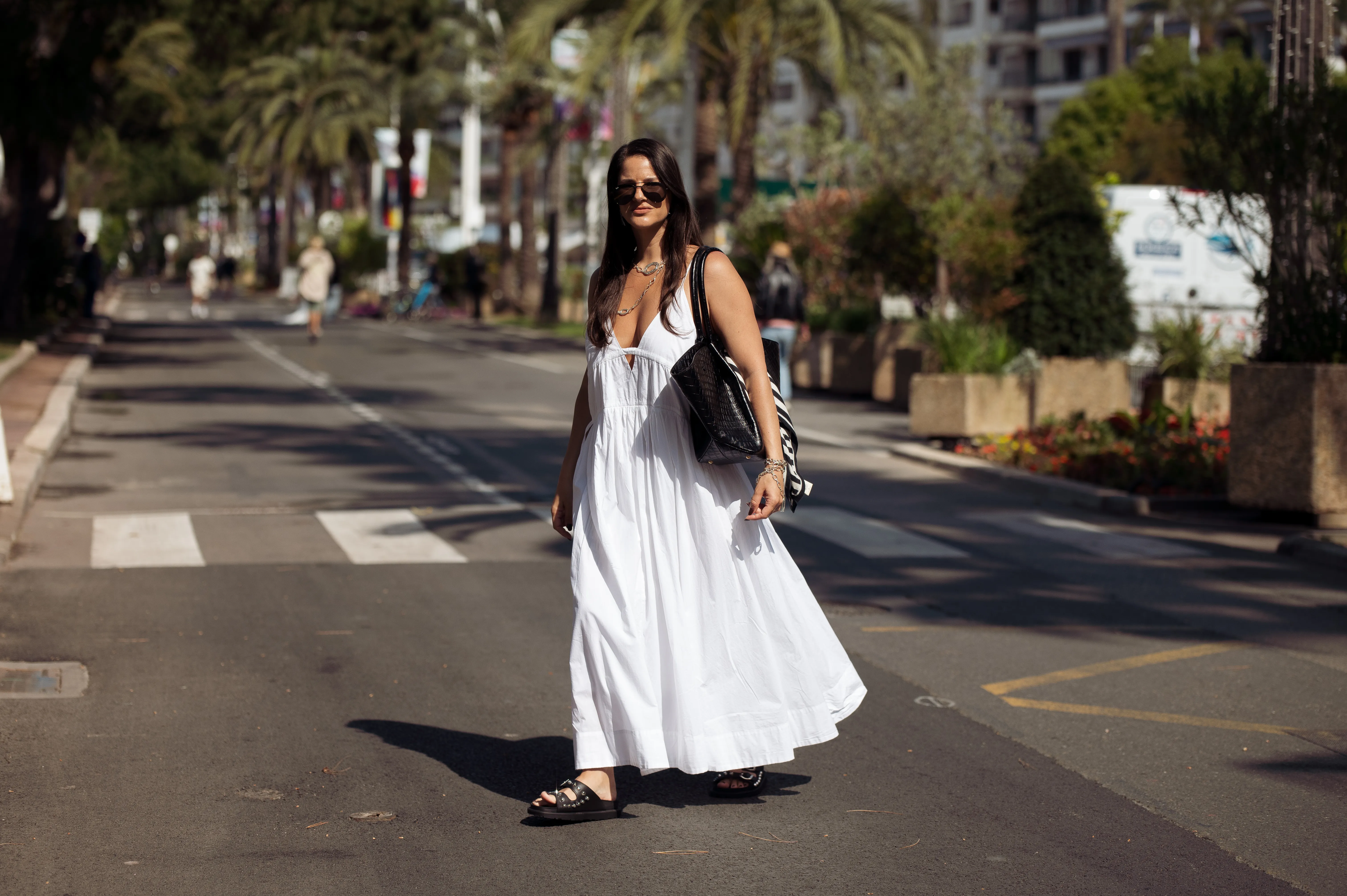 Gili Biegun wears a long white summer maxi dress, black bag with black and white scarf, silver necklaces, silver sea star earrings and black slippers with metal details during day five of the 78th Cannes Film Festival on May 17, 2025 in Cannes, France.