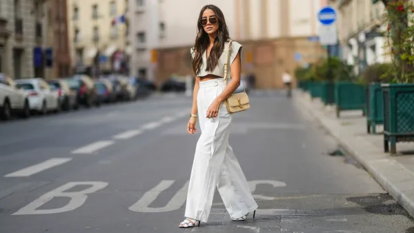 PARIS, FRANCE - APRIL 29: Tamara Kalinic wears gold Bottega Veneta sunglasses, a gold chain pendant necklace, a pale gray Jacquemus V-neck collar crop top with epaulets, white large flared Philosophy belted trousers pants, a gold Juste Un Clou Cartier bracelet, a gold Love Cartier bracelet, gold and silver Bee My Love Chaumet bracelets, a gold ring, a beige shiny leather Saint Laurent YSL shoulder bag, white shiny leather strappy heels Balenciaga sandals shoes, on April 29, 2021 in Paris, France. (Photo by Edward Berthelot/Getty Images)