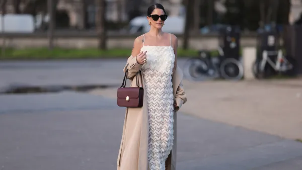 PARIS, FRANCE - FEBRUARY 27: Gili Biegun seen wearing YSL black sunglasses, Bottega Veneta gold tear drops earrings, white long sheer pearl embroidered maxi dress, gold statement rings, beige oversized long coat, Neous burgundy leather bag and burgundy varnished leather pumps / heels, outside Anrealage, during the Womenswear Fall/Winter 2024/2025 as part of Paris Fashion Week on February 27, 2024 in Paris, France. (Photo by Jeremy Moeller/Getty Images)