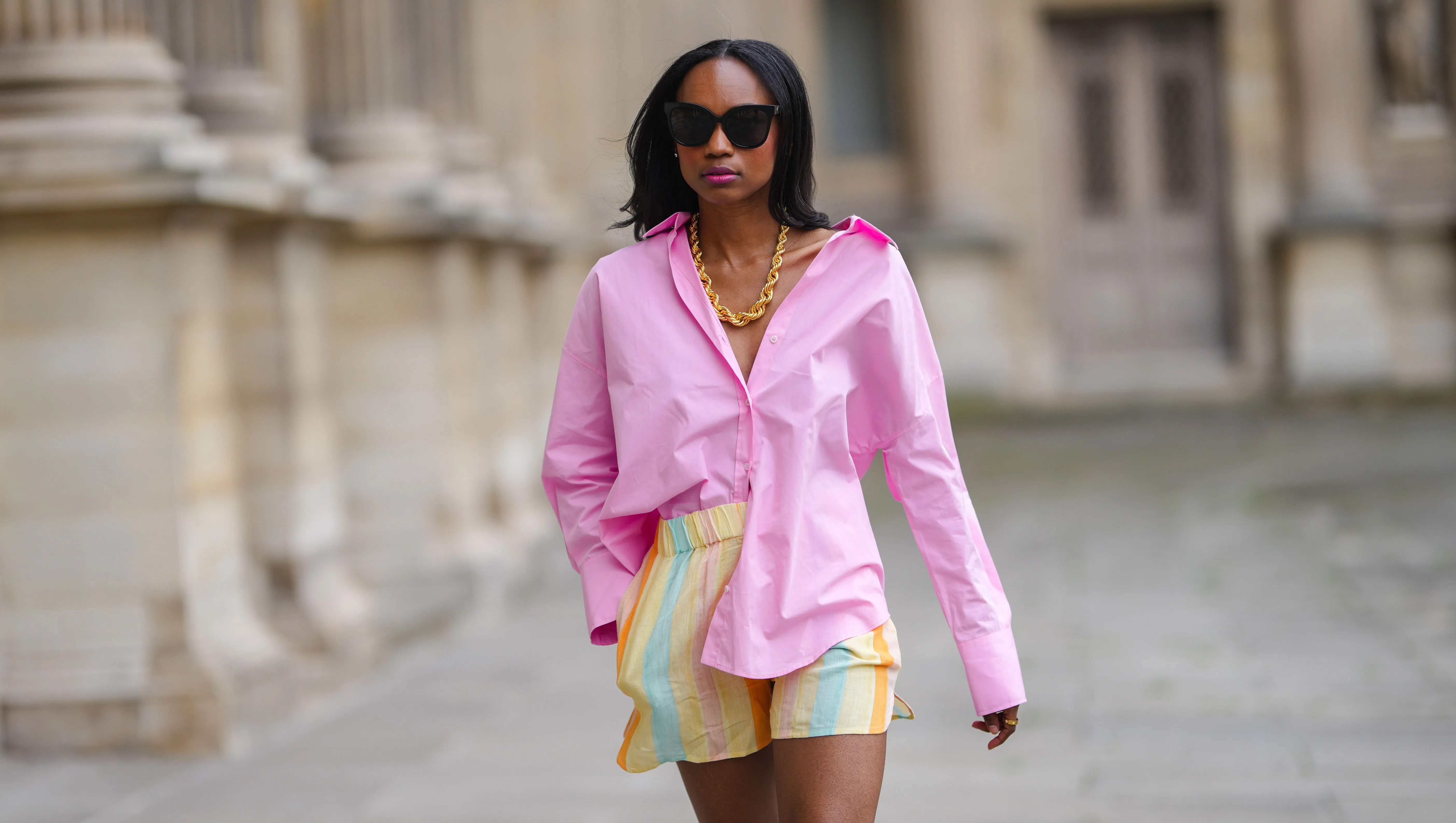 PARIS, FRANCE - JUNE 05: Emilie Joseph @in_fashionwetrust wears black sunglasses, silver earrings, a gold chunky necklace from Merbabe, a pale pink oversized boyfriend shirt worn off shoulder, a gold ring, large multicolor stripes pastel bower shorts, on June 05, 2021 in Paris, France. (Photo by Edward Berthelot/Getty Images)