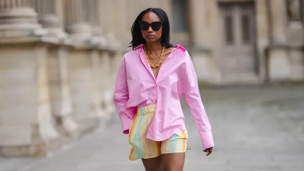 PARIS, FRANCE - JUNE 05: Emilie Joseph @in_fashionwetrust wears black sunglasses, silver earrings, a gold chunky necklace from Merbabe, a pale pink oversized boyfriend shirt worn off shoulder, a gold ring, large multicolor stripes pastel bower shorts, on June 05, 2021 in Paris, France. (Photo by Edward Berthelot/Getty Images)