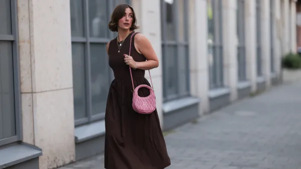 HAMBURG, GERMANY - JULY 18: Franzi Koenig is seen wearing several stud earrings, including gold seashell-shaped studs from fafe collection; layered gold necklaces with a seashell pendant, an F-letter pendant, and a white beaded necklace with a round organic-shaped pendant, also from fafe collection; a sleeveless dark brown midi dress with a ribbed top, high round neckline, and a gathered A-line skirt; a quilted pink leather “Wander” Hobo bag with gold logo hardware and a long thin shoulder strap from Miu Miu; several chunky gold rings, paired with delicate bracelets, both from fafe collection; and dark brown slip-on sandals with kitten heels on July 18, 2025 in Hamburg, Germany. (Photo by Jeremy Moeller/Getty Images)
