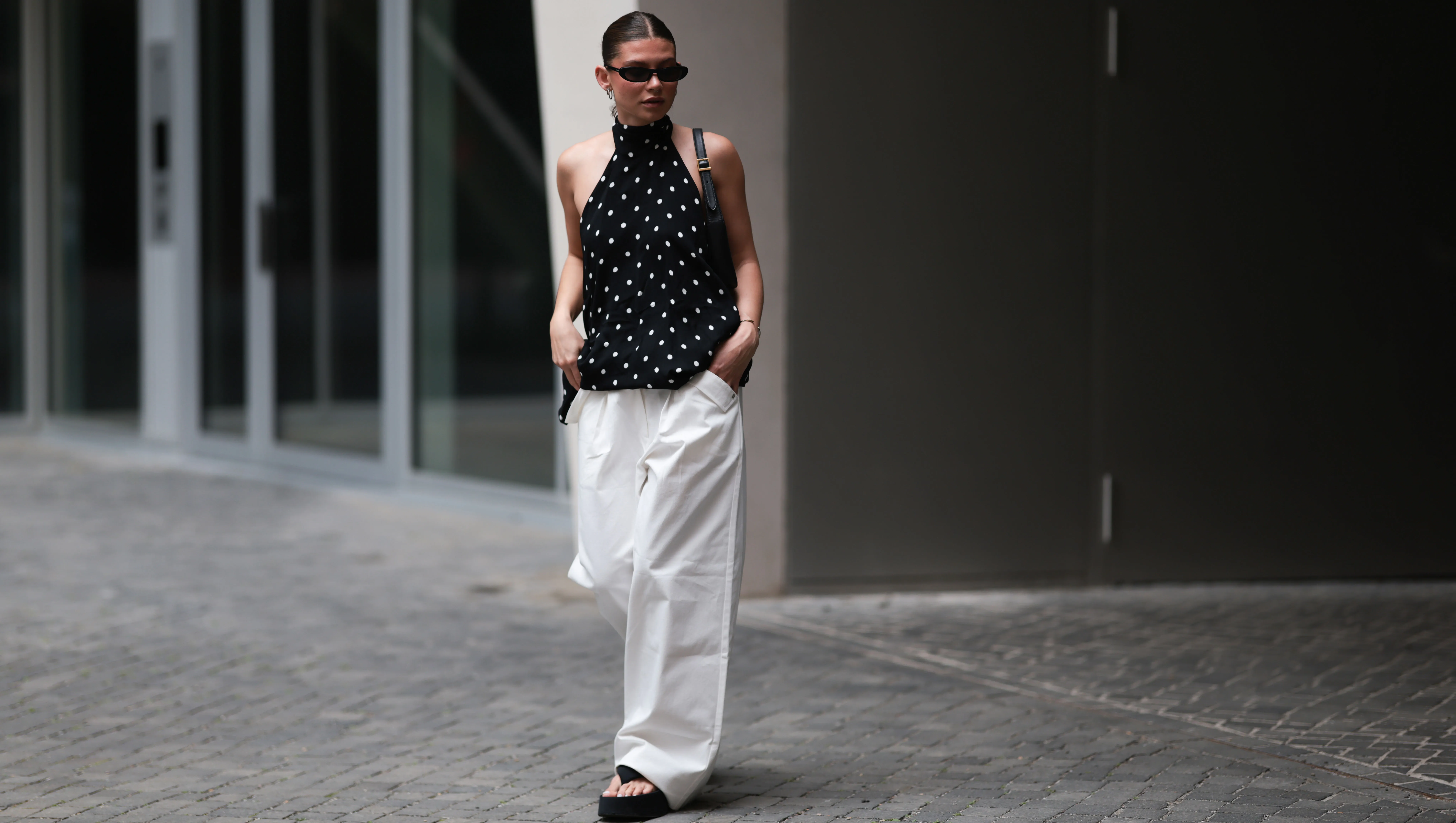 BERLIN, GERMANY - JUNE 04: Sophia Geiss is seen wearing silver hoop earrings in two different sizes; narrow oval black sunglasses from Saint Laurent; a silver nose ring; a flowy, backless halter-neck top in black with white polka dots from Zara; white wide-leg pants with a stretchy waistband and pocket details from The Room; a small rectangular black leather handbag with a gold YSL buckle from Yves Saint Laurent; a gold bangle; and black platform flip-flops from Zara on June 04, 2025 in Berlin, Germany. (Photo by Jeremy Moeller/Getty Images)