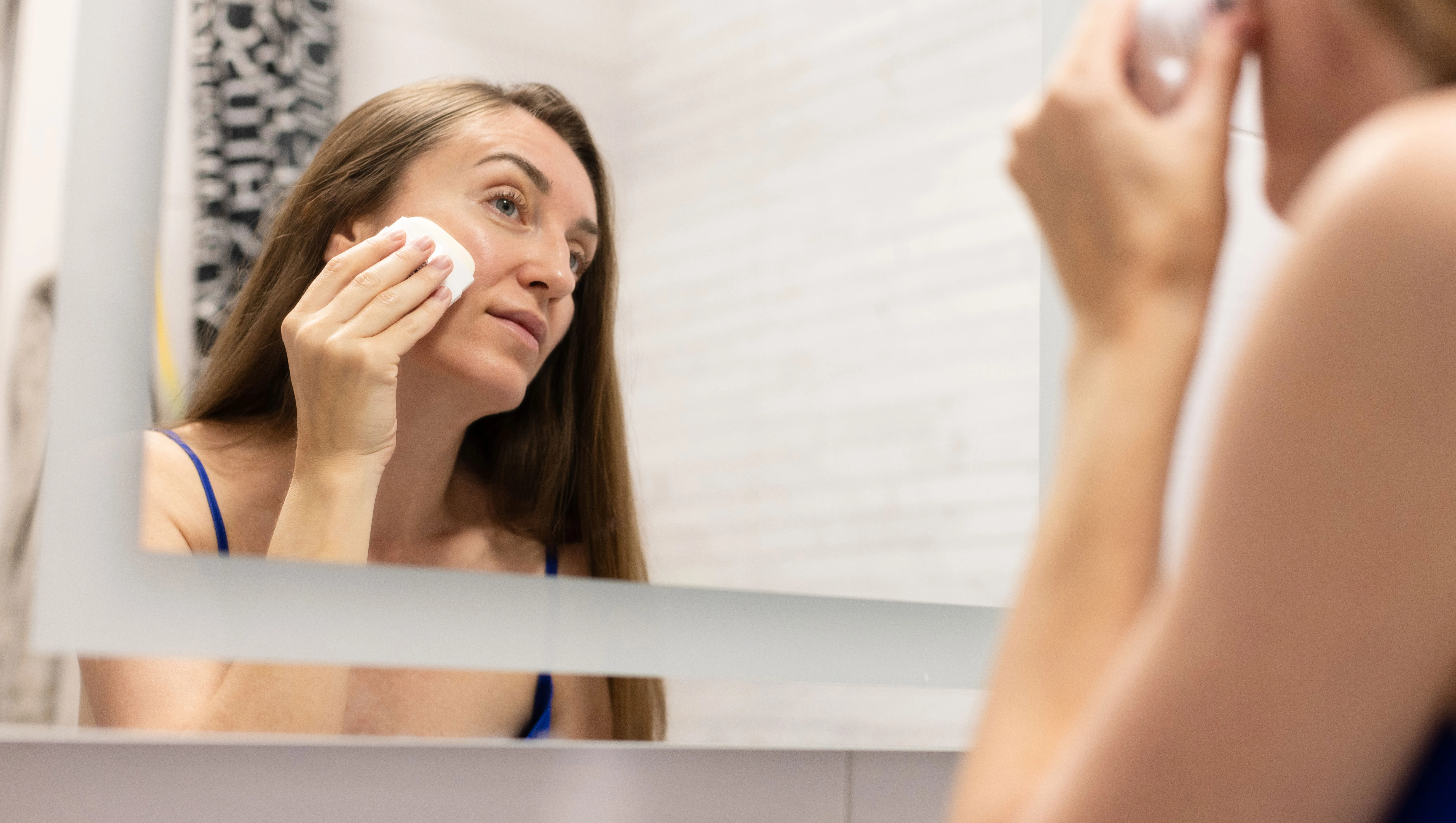 Smiling woman in front of mirror using cream stick for face.