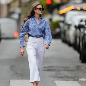 PARIS, FRANCE - MAY 20: Segolene Hyppolite wears sunglasses, a blue and white oversized shirt from Tommy Hilfiger, a raffia beige bag from Vanessa Bruno, high waist white denim pants from Vanessa Bruno, Chanel slingback shoes in blue denim with black tips, during a street style fashion photo session, on May 20, 2024 in Paris, France. (Photo by Edward Berthelot/Getty Images)