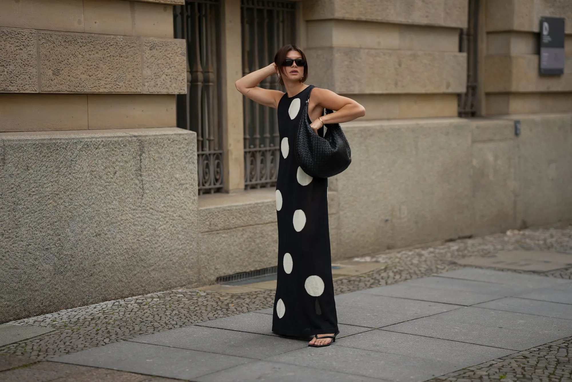 BERLIN, GERMANY - JUNE 24: Sophia Geiss is seen wearing a black and white long sleeveless polka dot knit dress with round neckline from Zara; a black Nana leather hobo bag with braided structure from abro; black PR 25YS sunglasses with rectangular biker shape from Prada; a pair of black thong sandals with kitten heel from LeGer by Lena Gercke; a pair of silver Harmonie big hoop earrings from black palms the label; a thin gold bangle from Daniel Wellington on June 24, 2025 in Berlin, Germany. (Photo by Moritz Scholz/Getty Images)