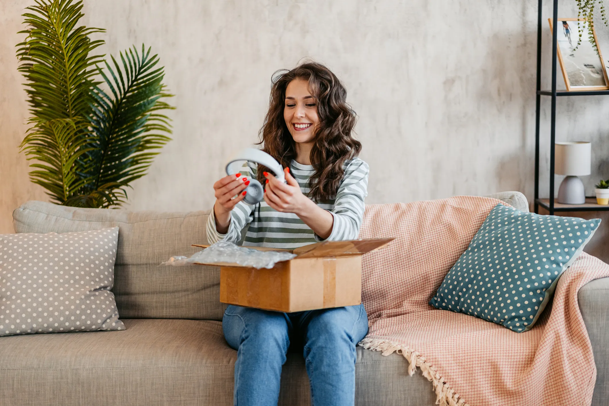 Beautiful mature woman unboxing a package with new headphones she ordered online at home.
