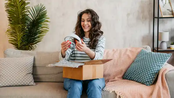 Beautiful mature woman unboxing a package with new headphones she ordered online at home.