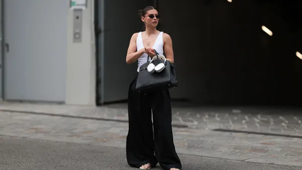 BERLIN, GERMANY - JUNE 04: Sophia Geiss is seen wearing silver hoop earrings in two different sizes; oval, rimless black sunglasses from Vehla Eyewear; a silver nose ring; a white sleeveless bodysuit with a deep neckline from Zara; pleated wide-leg black suit pants from COS; a large rectangular black leather handbag from DeMellier; a gold bangle paired with a chunky beige bangle; and white flip-flops from Havaianas, while holding silver Apple AirPods Max headphones on June 04, 2025 in Berlin, Germany. (Photo by Jeremy Moeller/Getty Images)
