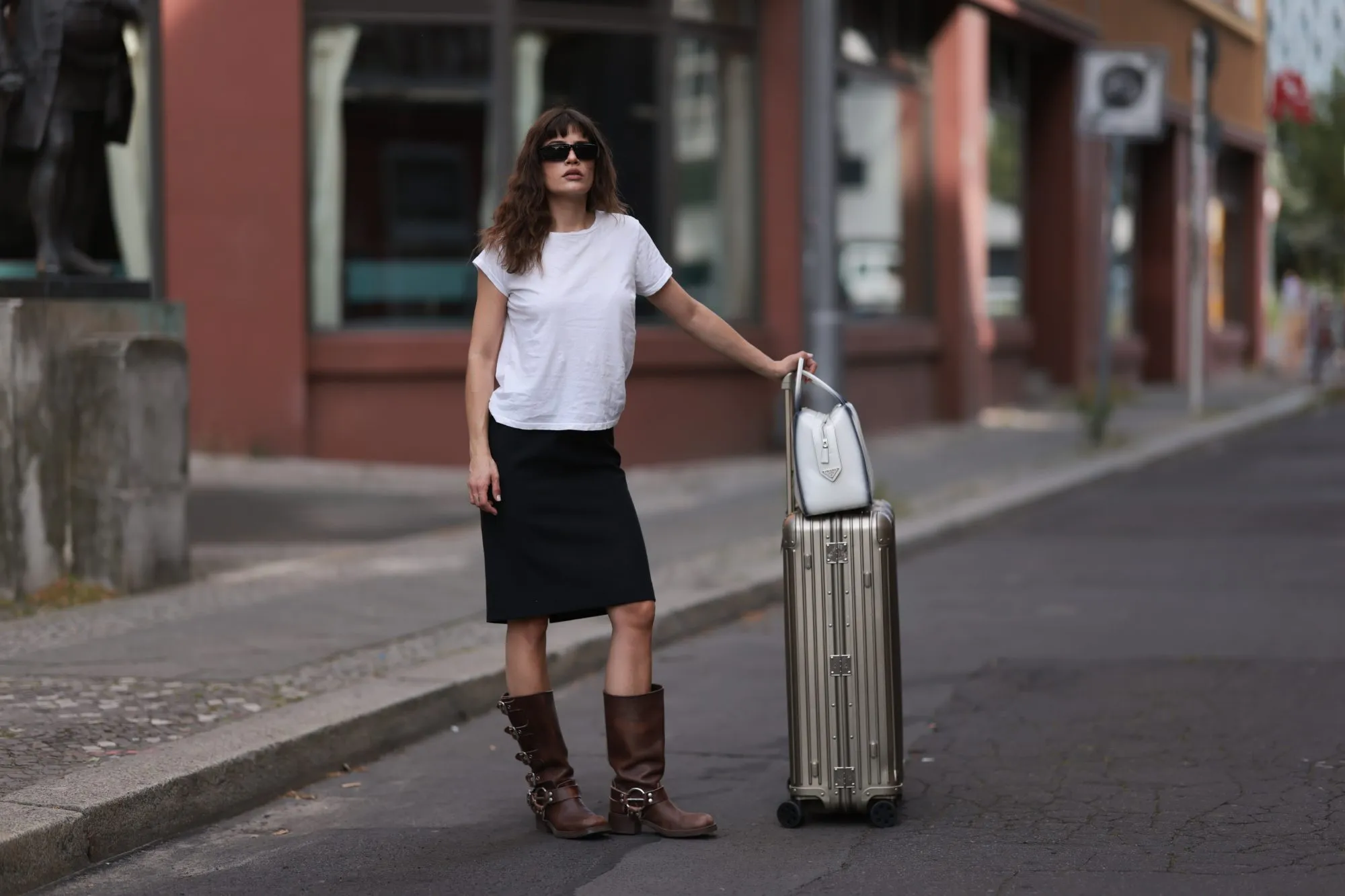 BERLIN, GERMANY - JULY 11: Lea Naumann is seen wearing black sunglasses from Prada, a white tee from Mother Denim, a black knee-length vintage skirt, brown leather boots with silver buckle closure from Miu Miu, a white leather Supernova bag from Prada and a silver suitcase from Rimowa on July 11, 2023 in Berlin, Germany. (Photo by Jeremy Moeller/Getty Images)
