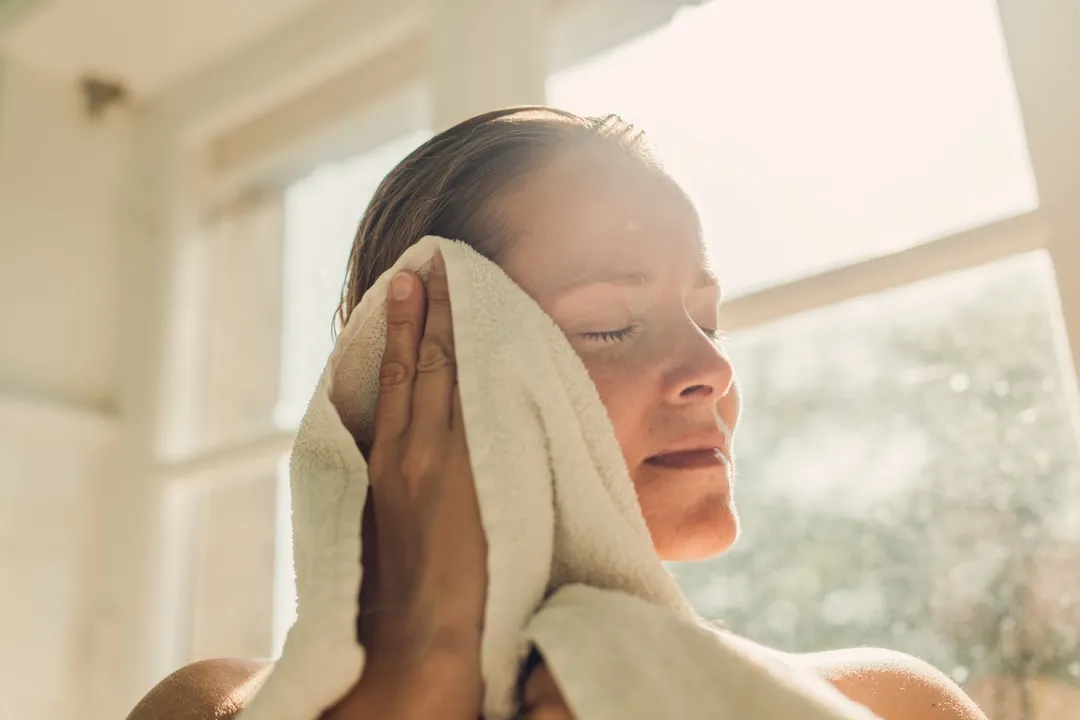 Woman toweling oneself off after bathing in sunny bathroom.