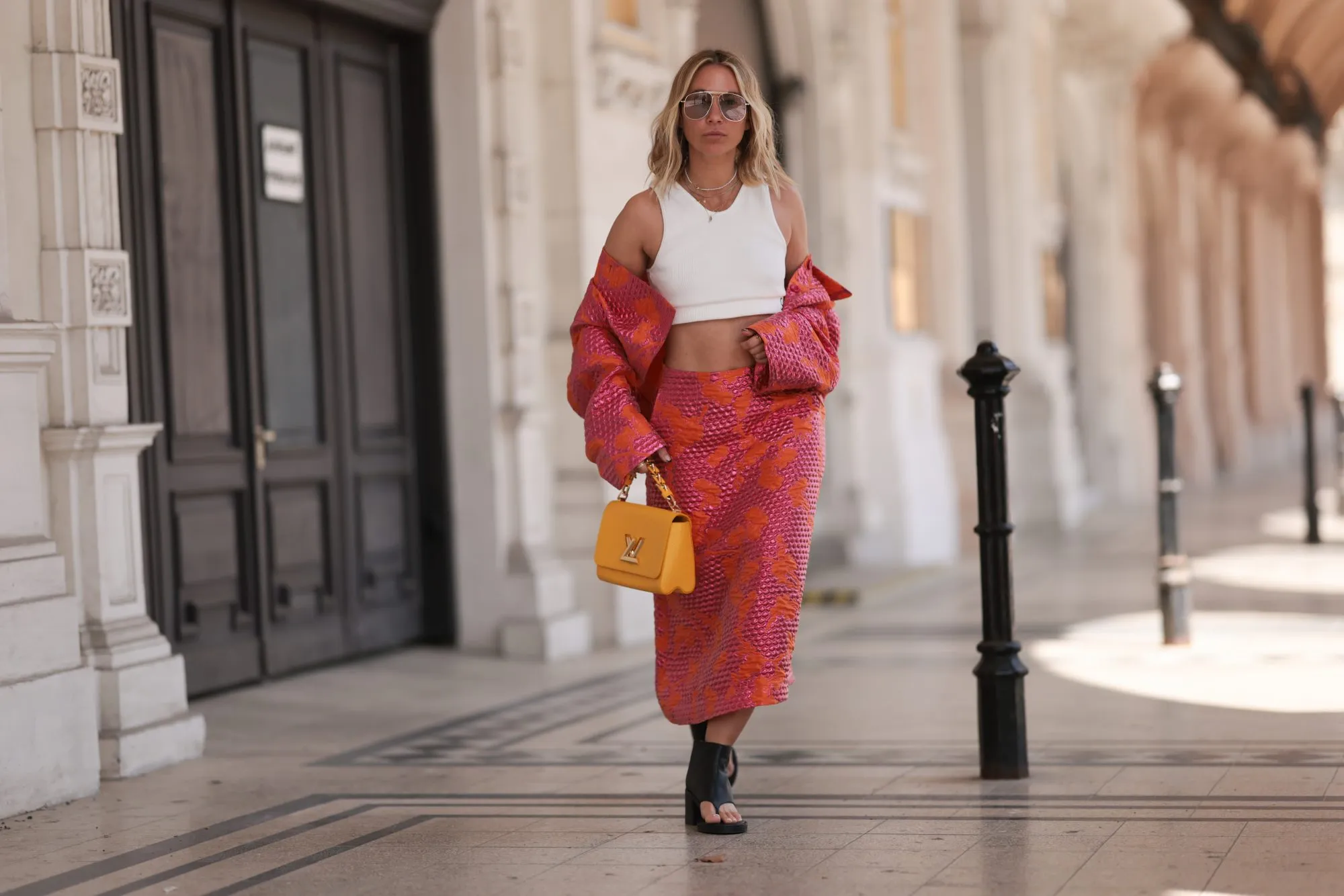 VIENNA, AUSTRIA - MAY 01: Karin Teigl wearing Baum & Pferdgarten matching cropped colorful shiny pink orange jacket and long midi skirt, Miu Miu black leather thong ankle boots, CYK white cropped bra top, Tom ford round gold glasses and Louis Vuitton yellow leather Twist bag on May 01, 2023 in Vienna, Austria. (Photo by Jeremy Moeller/Getty Images)