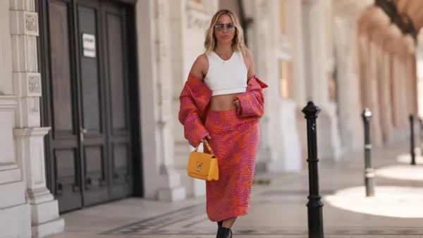 VIENNA, AUSTRIA - MAY 01: Karin Teigl wearing Baum & Pferdgarten matching cropped colorful shiny pink orange jacket and long midi skirt, Miu Miu black leather thong ankle boots, CYK white cropped bra top, Tom ford round gold glasses and Louis Vuitton yellow leather Twist bag on May 01, 2023 in Vienna, Austria. (Photo by Jeremy Moeller/Getty Images)