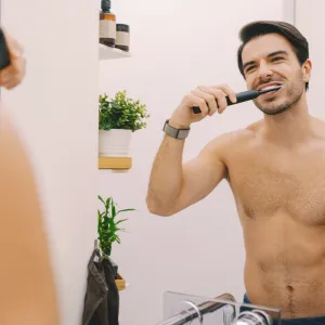Мan in the bathroom is brushing his teeth with electric toothbrush