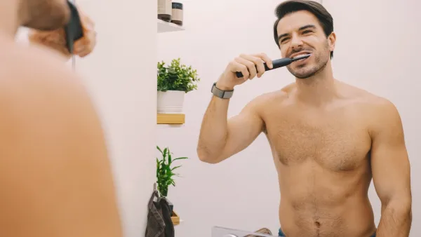 Мan in the bathroom is brushing his teeth with electric toothbrush