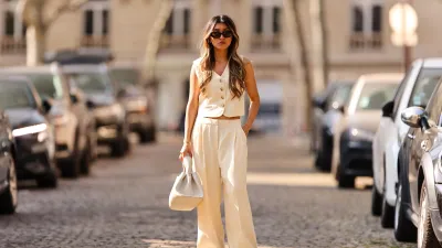 PARIS, FRANCE - MARCH 26: Angela Gonzalez wears black sunglasses, silver earrings, a white latte buttoned / sleeveless / linen gilet, matching white latte palazzo pants, a white matte leather handbag, white and dark green details leather sneakers from New Balance, during a street style fashion photo session, on March 26, 2022 in Paris, France. (Photo by Edward Berthelot/Getty Images)