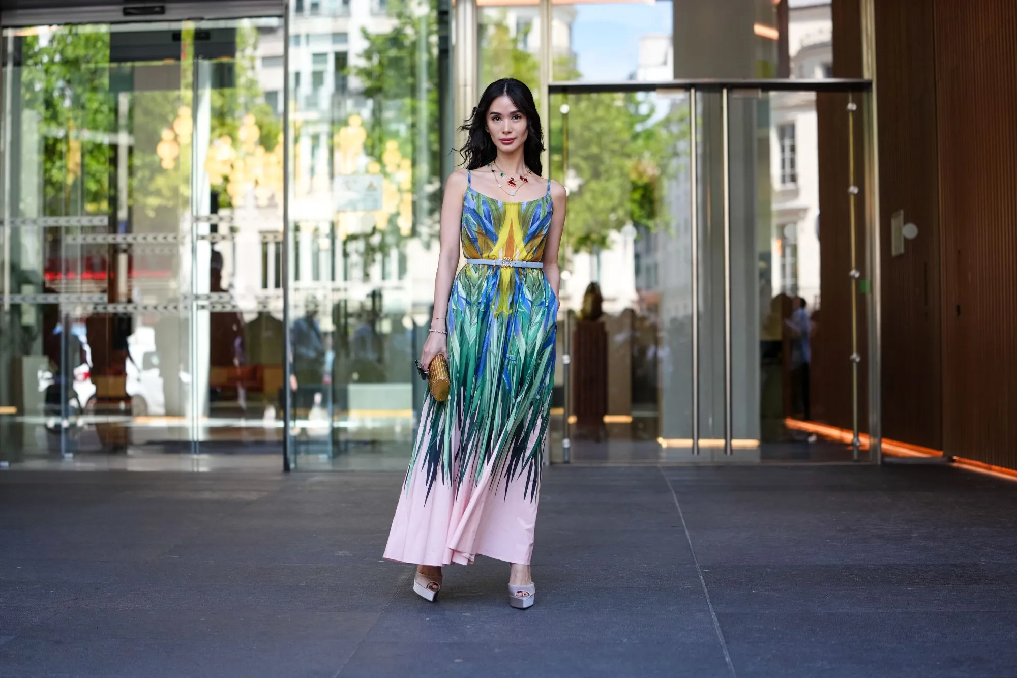 PARIS, FRANCE - JULY 09: Heart Evangelista wears a sleeveless maxi dress featuring a vibrant, multicolored abstract pattern with shades of blue, green, yellow, and pink. The dress has thin straps and a fitted bodice, transitioning into a flowing skirt. A thin belt in a neutral tone cinches the waist. Accessories include a gold-toned clutch with a textured surface and a statement necklace with red accents. Footwear consists of light-colored platform heels. Hair is styled in loose waves, and makeup is subtle with a focus on natural tones, outside Elie Saab, during Paris Fashion Week - Haute Couture Fall/Winter 2025/2026, on July 09, 2025 in Paris, France (Photo by Edward Berthelot/Getty Images)