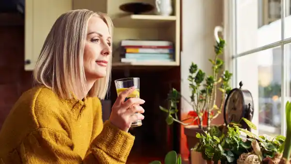 Mature woman drinking glass of water in the kitchen looking through the window