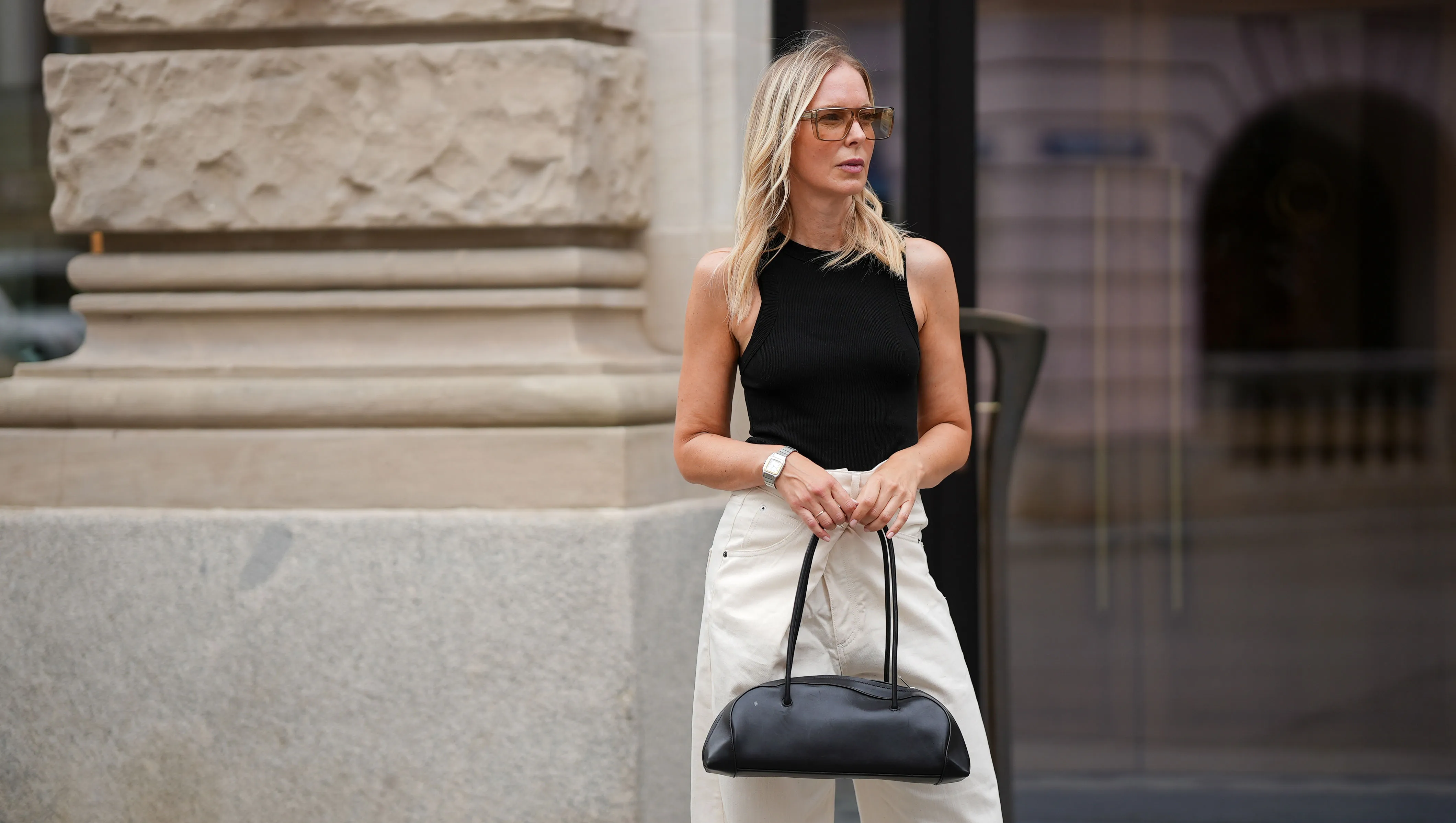 MUNICH, GERMANY - JULY 3: Mirja Klein is seen wearing a black high neck cotton tanktop from COS; washed white Ines denim trousers with fold-over closure and wide leg silhouette from DARKPARK; a black Eastside leather bowling bag with elongated shape from COS; transparent sunglasses with slightly brown colored acetate frame and glasses in rectangular shape from Saint Laurent; a vintage silver-golden bicolor Santos de Cartier wristwatch from Cartier on July 3, 2025 in Munich, Germany. (Photo by Moritz Scholz/Getty Images)