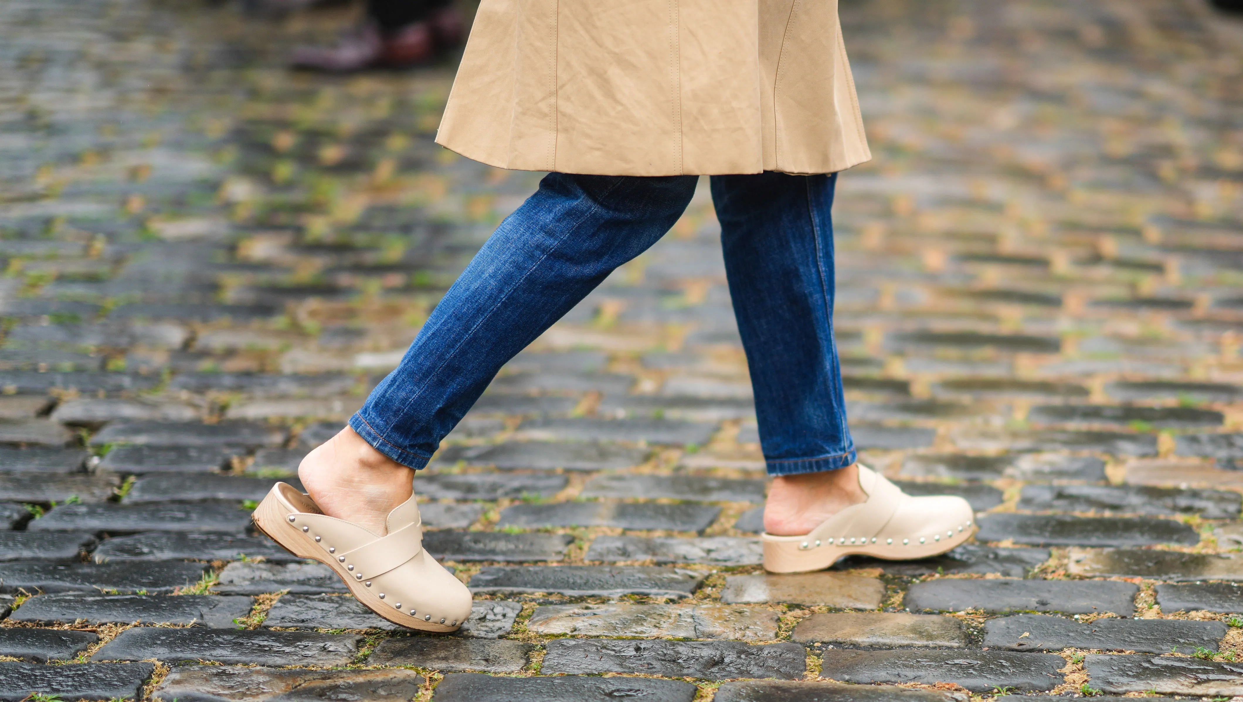 PARIS, FRANCE - JUNE 26: A guest wears a long beige trench coat, blue flared denim jeans pants, beige nailed / studded mules shoes, outside Hermes, during Paris Fashion Week - Menswear Spring/Summer 2022, on June 26, 2021 in Paris, France. (Photo by Edward Berthelot/Getty Images)