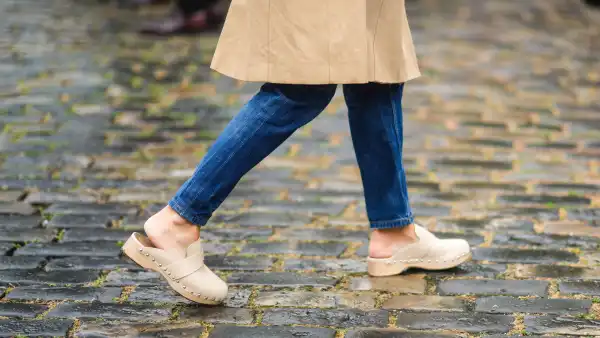 PARIS, FRANCE - JUNE 26: A guest wears a long beige trench coat, blue flared denim jeans pants, beige nailed / studded mules shoes, outside Hermes, during Paris Fashion Week - Menswear Spring/Summer 2022, on June 26, 2021 in Paris, France. (Photo by Edward Berthelot/Getty Images)