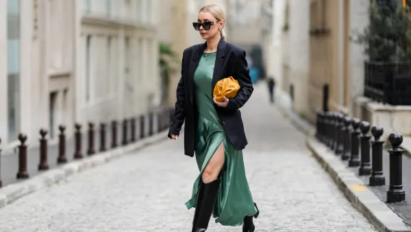 PARIS, FRANCE - JANUARY 25: Justyna Czernia wears sunglasses, gold earrings, a green mint satin silk slit / split long dress, a black oversized blazer jacket, an orange shiny leather puffy handbag from Bottega Veneta, black shiny leather pointed high boots, gold ring, outside Alexis Mabille, during Paris Fashion Week - Haute Couture Spring/Summer 2022, on January 25, 2022 in Paris, France. (Photo by Edward Berthelot/Getty Images)