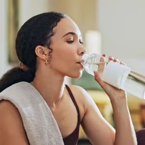 Woman, exercise and drinking water on floor in home with thinking, hydration or liquid for health detox. Girl, person and bottle for workout, nutrition and wellness with training for fitness in house