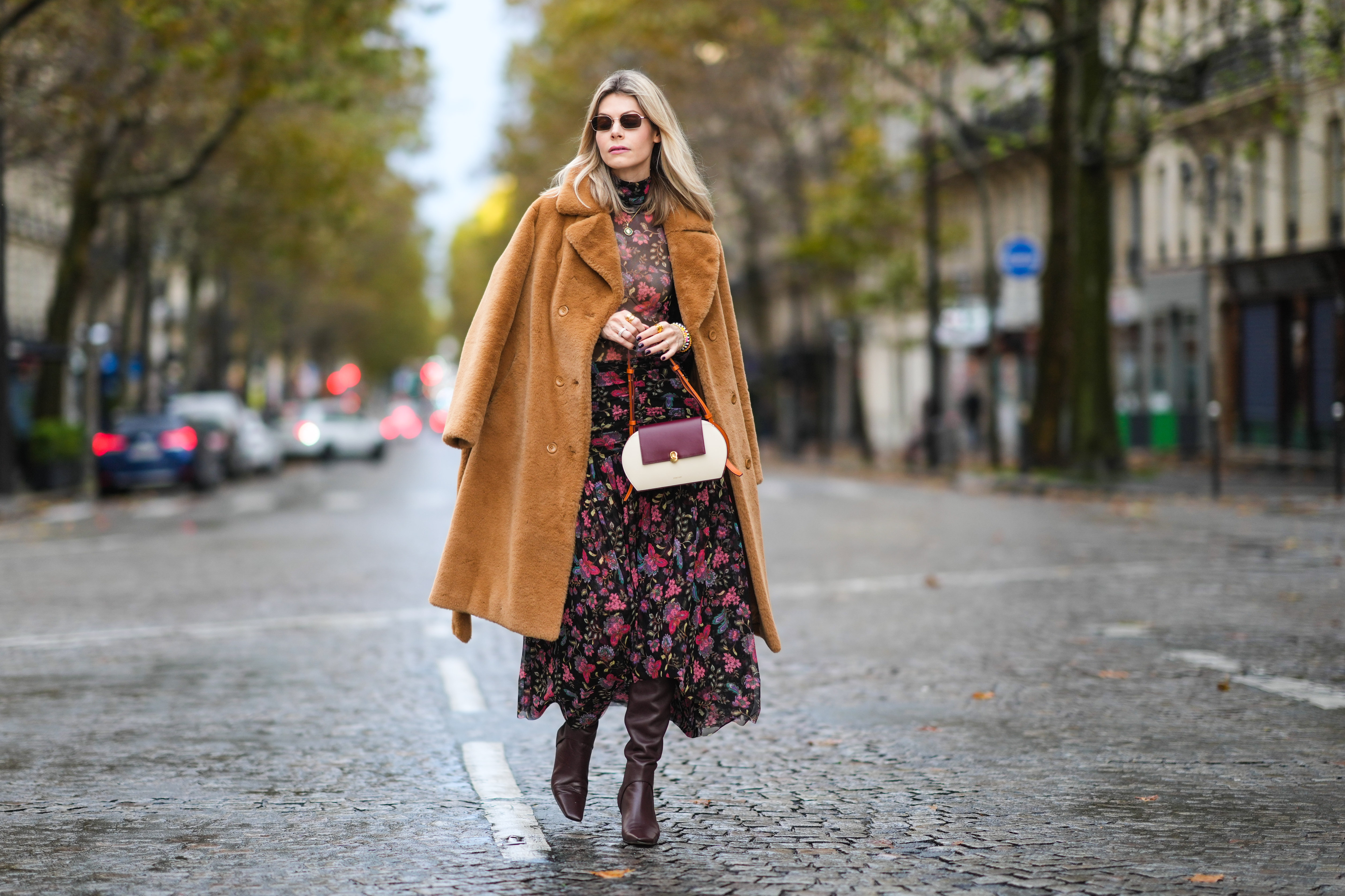 Kate Tik wears black sunglasses, a black with red / purple / green flower print pattern turtleneck transparent long sleeves t-shirt form Misa Los Angeles , a matching black with red / purple / green flower print pattern high waist long skirt from Misa Los Angeles, a brown oversized fluffy long coat from Stand Studio, multicolored pearls bracelets, gold rings, a burgundy / camel / white latte matte leather yoke handbag from Noirgaze, brown shiny leather pointed heels knees boots from Neil J Rogers, during a street style fashion photo session, on October 31, 2021 in Paris, France.