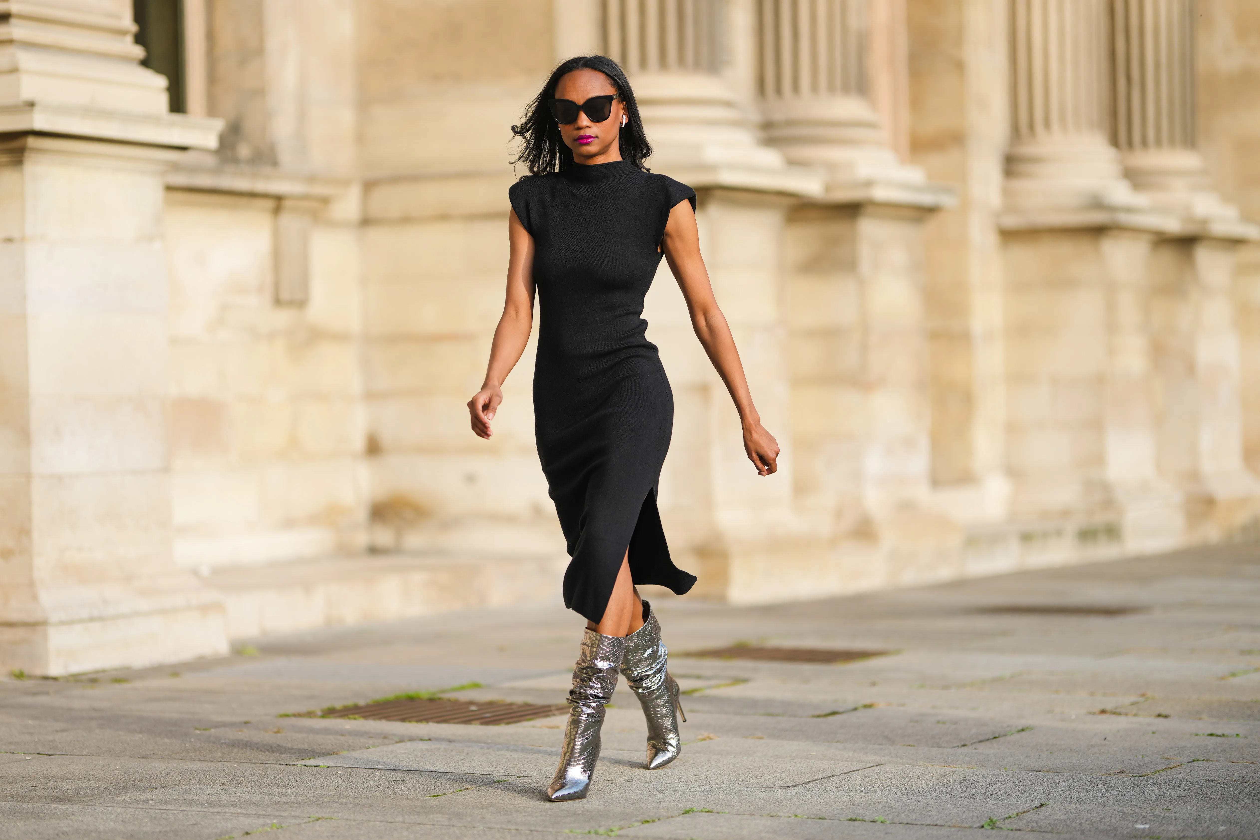 Emilie Joseph @in_fashionwetrust wears black vintage sunglasses, rhinestones earrings, a black woolblend knit dress with epaulets Slit detail from Midlength, silver python effect leather slouchy boots by Paris Texas, during a street style fashion photo session, on November 07, 2021 in Paris, France.